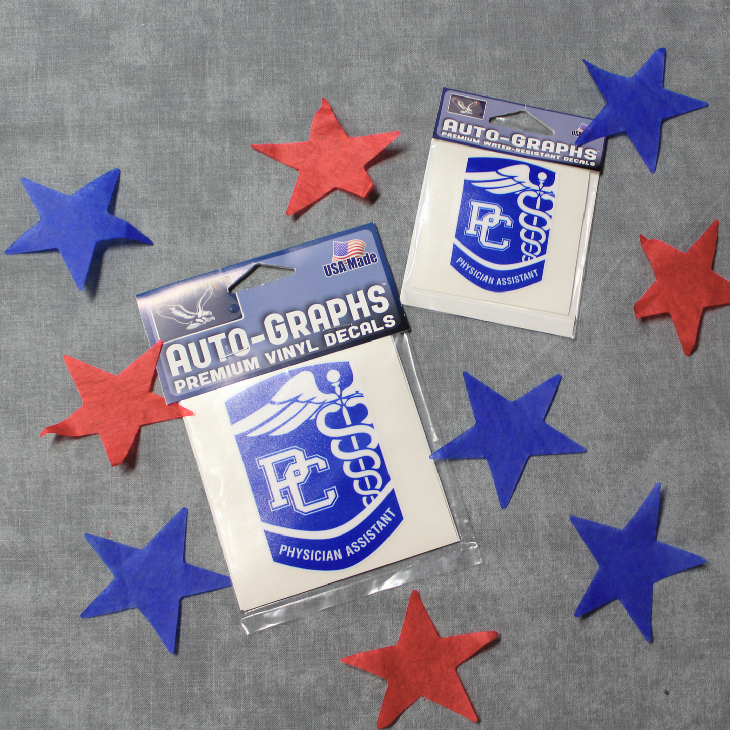 Picture with the two sizes of the PC Physician Assistant Decals. The decals are stylized as the PC PA badge and are royal blue with white details. The background of the photo has red and blue stars surrounding the decals.