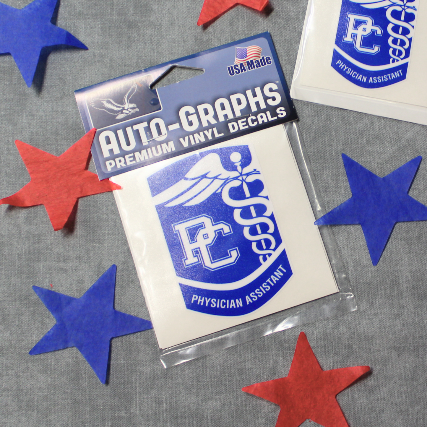 Picture featuring the large PC Physician Assistant Decal. The decals are stylized as the PC PA badge and are royal blue with white details. The background of the photo has red and blue stars surrounding the decals.