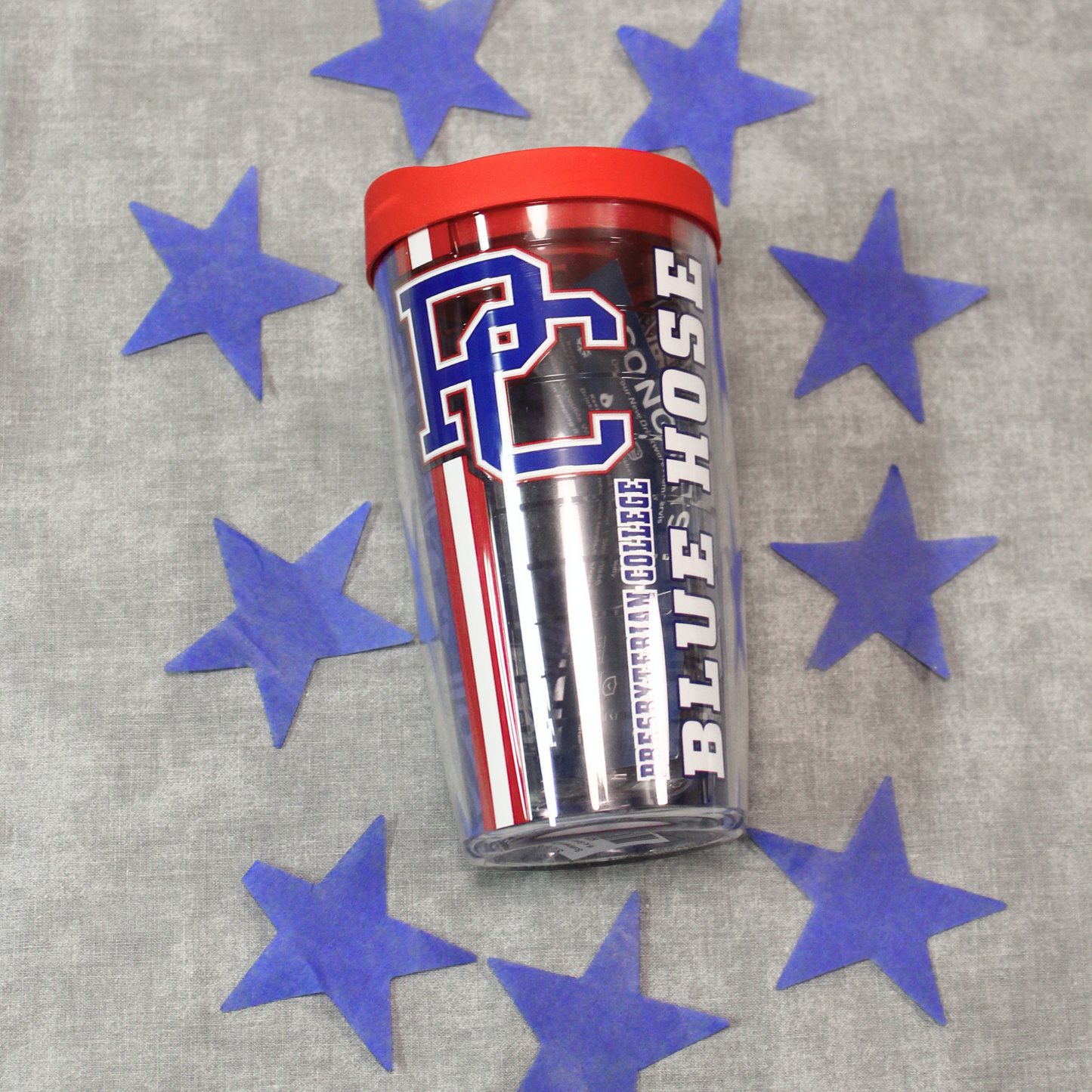 Tervis tumbler 16oz with a block PC logo, Presbyterian College, and Blue Hose printed on it in white, blue, and red inks. The cup features a red lid. The background of the image features blue stars.