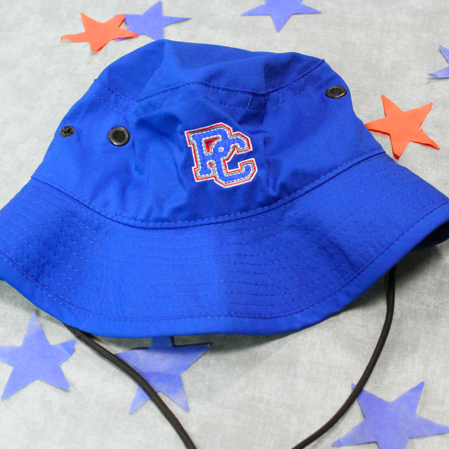 Royal Blue Boonie Hat with strap and embroidered PC logo in red, white, and blue thread on the front of the hat. The background of this photo has red and blue stars.