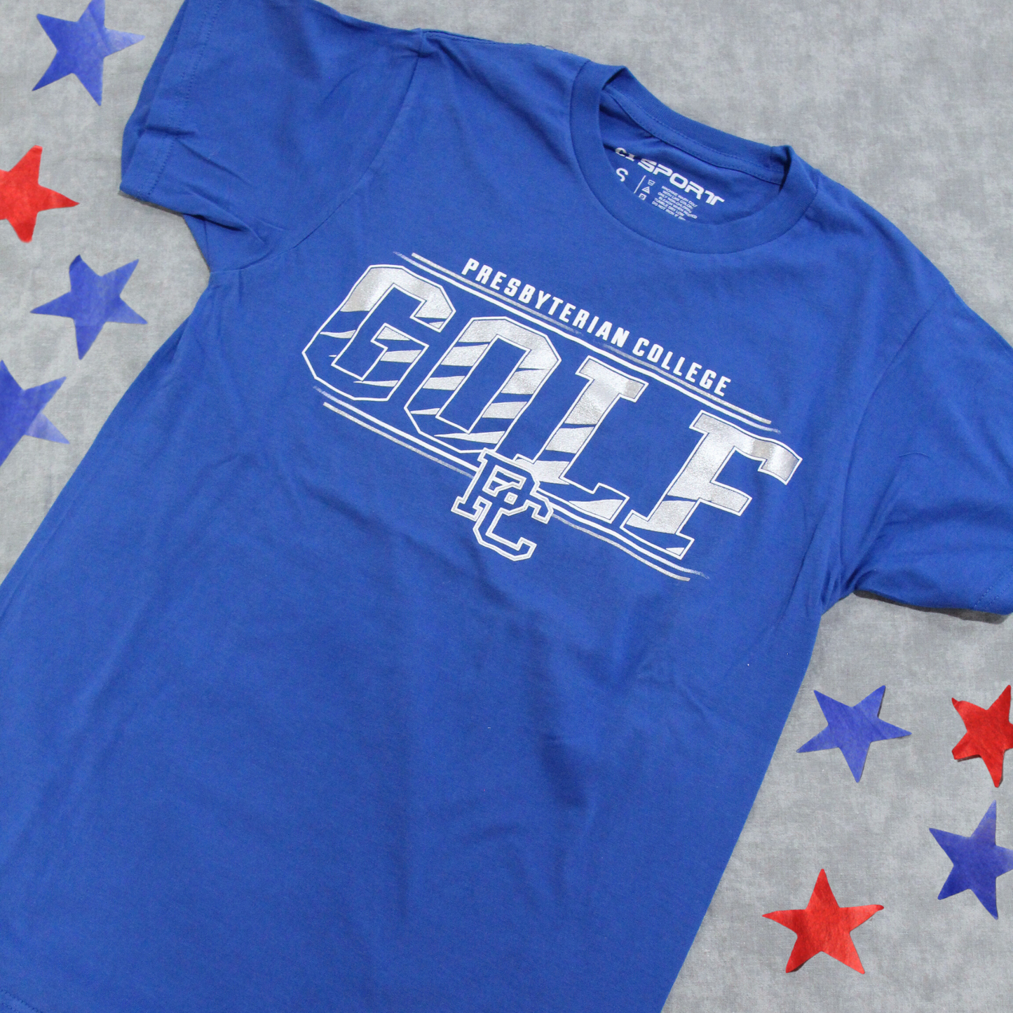 Product photo of a royal blue t-shirt with a silver ink screen print graphic "Presbyterian College Golf". This product photo has red and blue stars on the background.