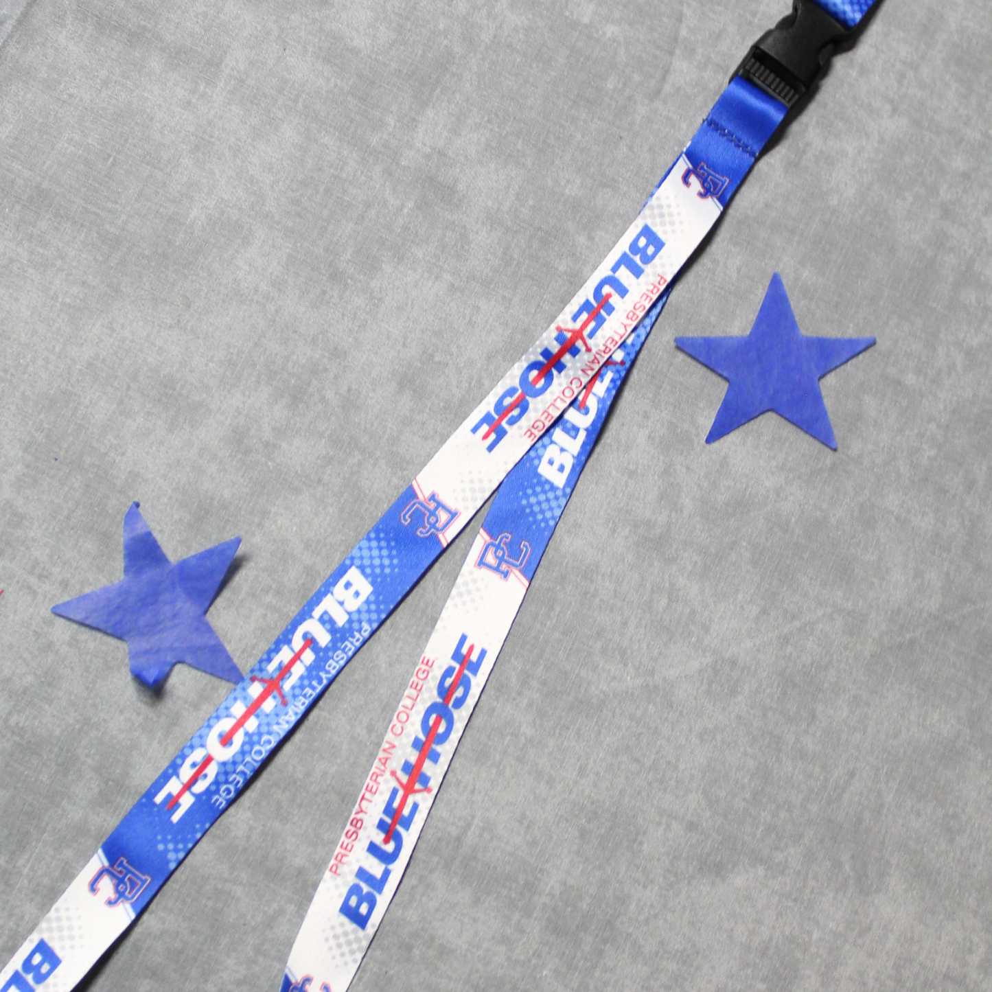 A royal blue and white 3/4 inch lanyard with Presbyterian College, PC logo, and the Blue Hose athletic wordmark printed on it. The lanyard features a buckle so you can separate the key ring from the lanyard if need be. The background of this image has two blue stars on it.
