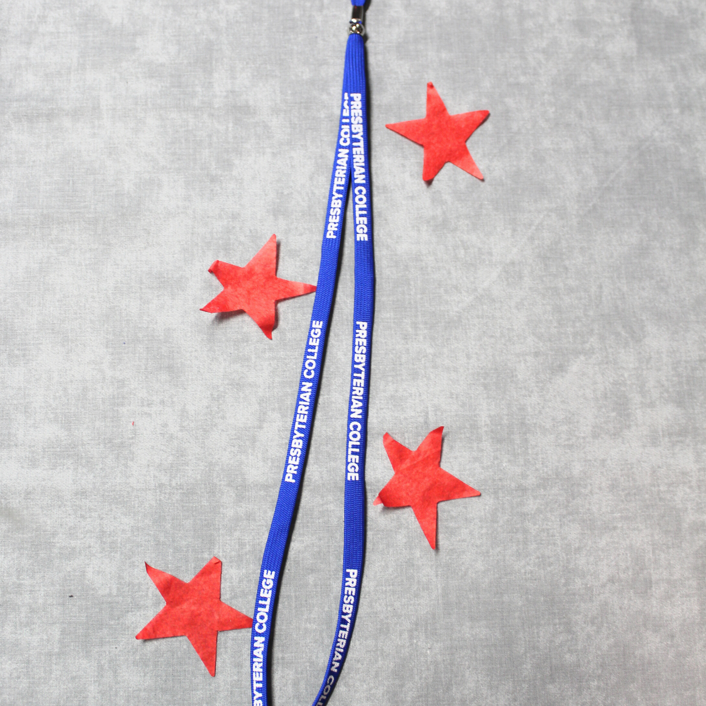 Product photo of a royal blue lanyard with white lettering printed on it that spells out Presbyterian College. Background of the photo has red stars surrounding the lanyard.