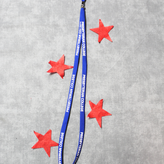 Product photo of a royal blue lanyard with white lettering printed on it that spells out Presbyterian College. Background of the photo has red stars surrounding the lanyard.