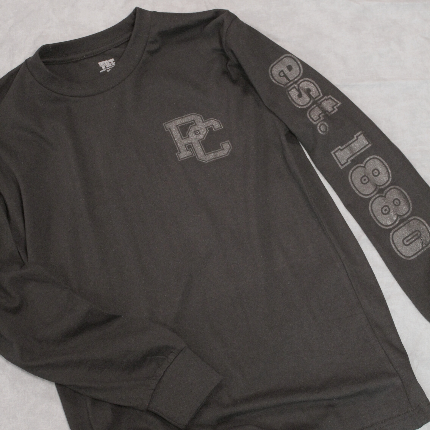 Black ink on a black long sleeve shirt. The left sleeve features "est. 1880" and left front chest has a PC logo printed on it.