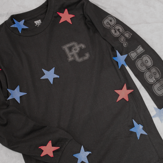 Black ink on a black long sleeve shirt. The left sleeve features "est. 1880" and left front chest has a PC logo printed on it. This product photo has red and blue paper stars across the shirt.