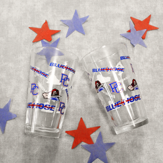 Another view of the two drinking glasses that feature the PC logo, Scotty the Scotsman Athletic logo, and the Blue Hose wordmark logo. Background features blue and red stars.