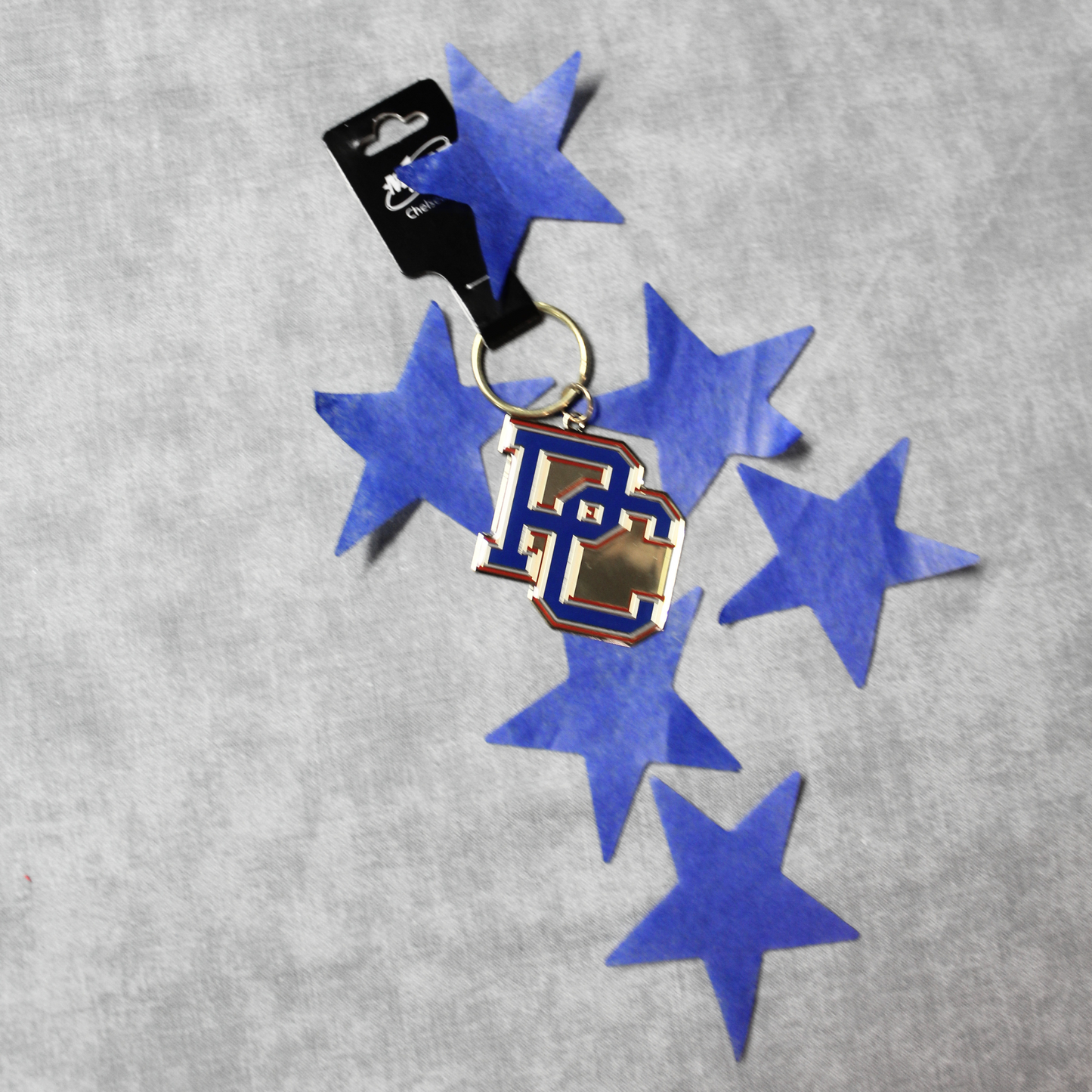 A picture of the brass keychain that features a blue, red, and white block PC logo in front of a backdrop of blue stars.