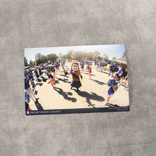 Another picture of the Bailey Stadium Cheer Postcard that features Scotty the Scotsman Mascot carrying a sword surrounded by the Presbyterian College Cheer team and fans out front of the football stadium. This picture has a plain grey background that the postcard sits on top.