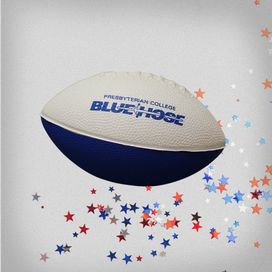 Photo of a small white and royal blue foam football with the Presbyterian College Blue Hose athletic wordmark printed across the top of the football in royal blue ink. The backdrop has red, white, and blue stars in the bottom right corner.