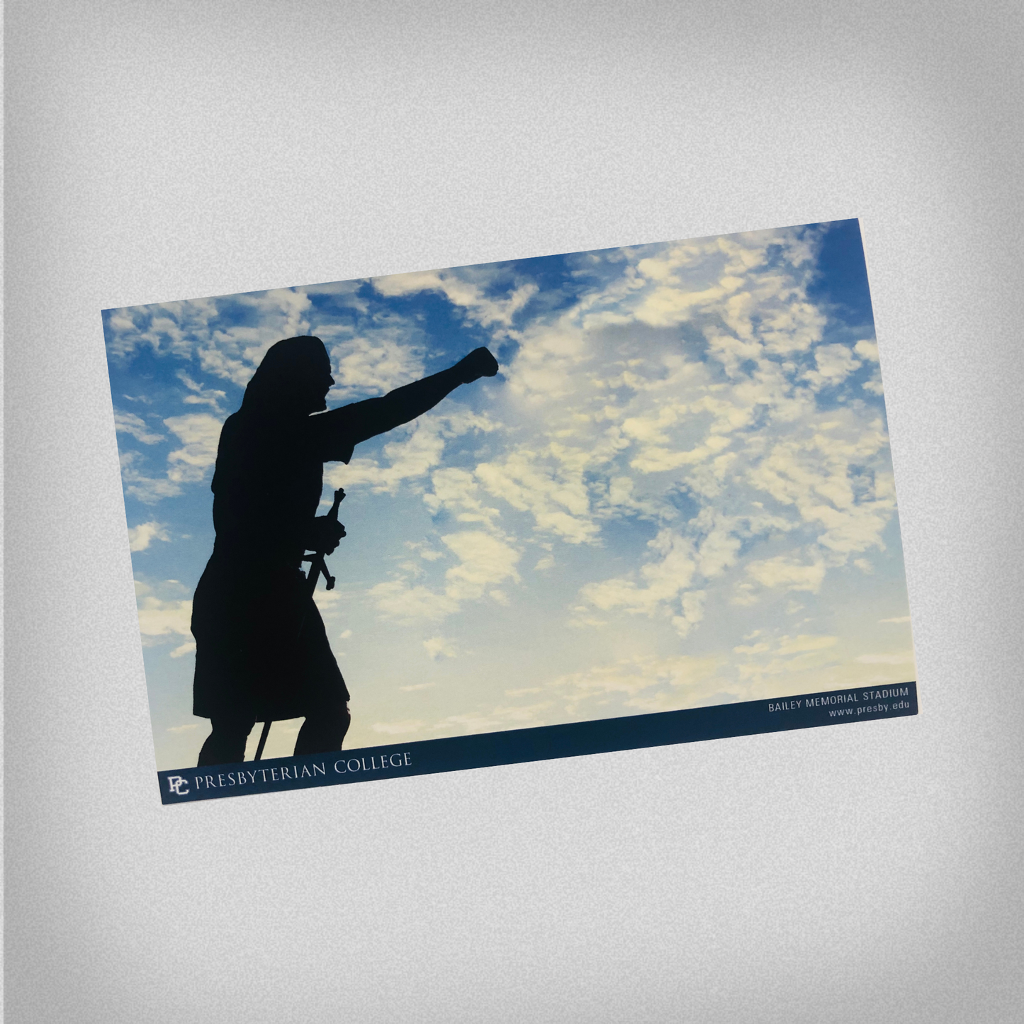 Postcard that features the silhouette of the statue of Cyrus the Scotsman from in front of Bailey Stadium against a background of a cloudy sky.