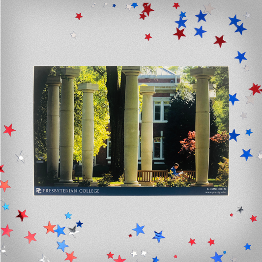 The alumni green postcard has a picture of the columns that mark the Alumni Green spot on campus with a student studying on a bench between the columns. The background of this product photo has blue, white, and red stars on it.
