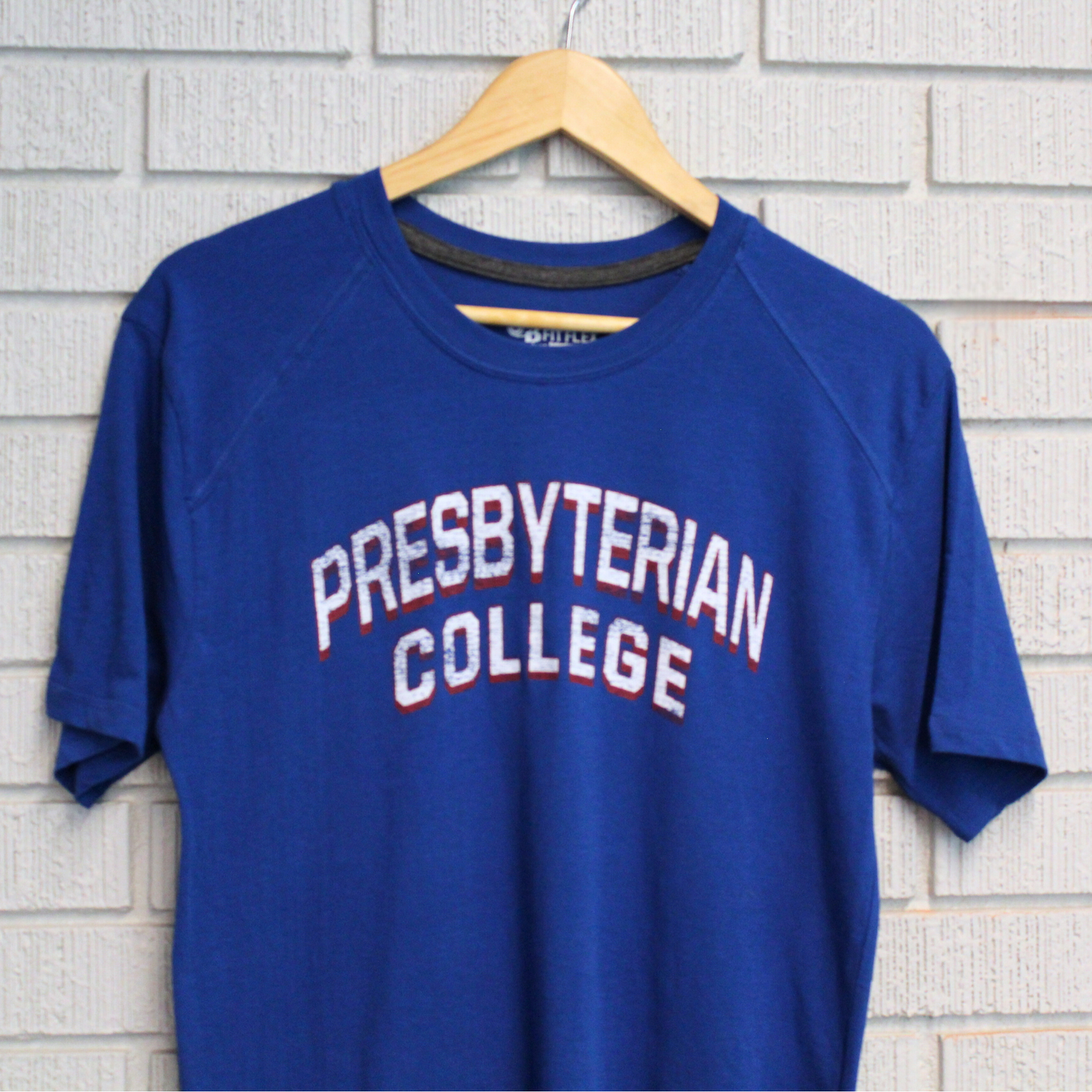 Photo of a royal blue fit flex t-shirt with a distressed screen print graphic in white and red ink of "Presbyterian College"