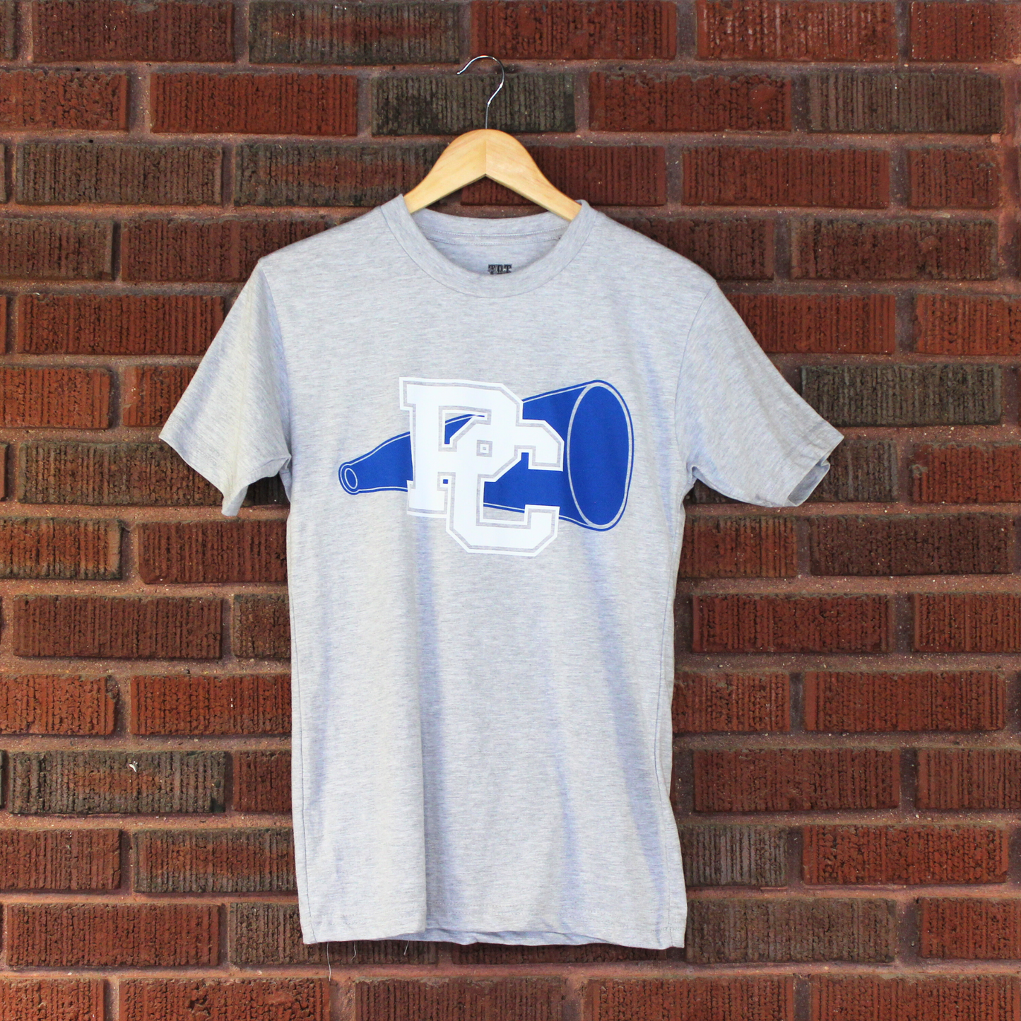 Product photo of a light grey t-shirt with a royal blue megaphone on it and a white block PC logo.
