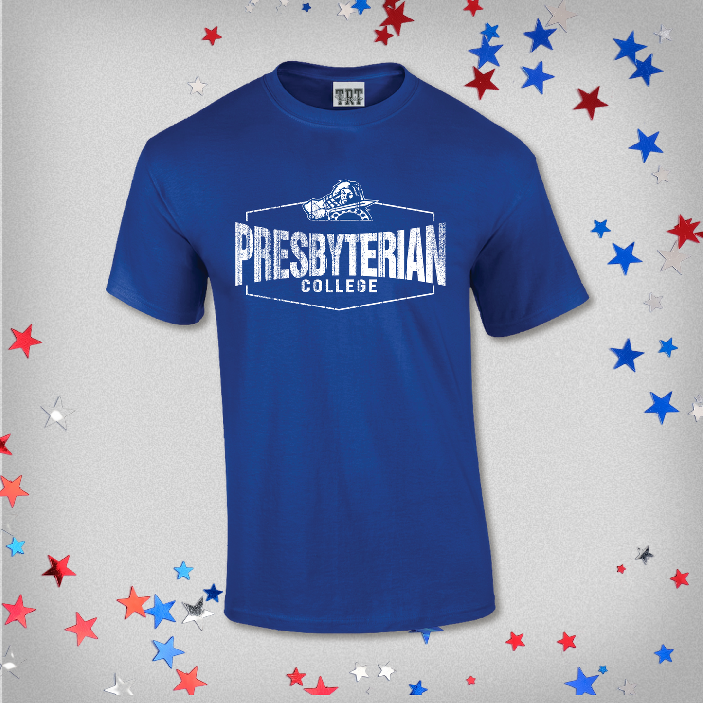 Product photo of a royal blue shirt with white ink distressed screen print graphic that features a hexagon with Presbyterian College inside it and the Scotty the Scotsman athletic mark. The background of this product photo has red, white, and blue stars.