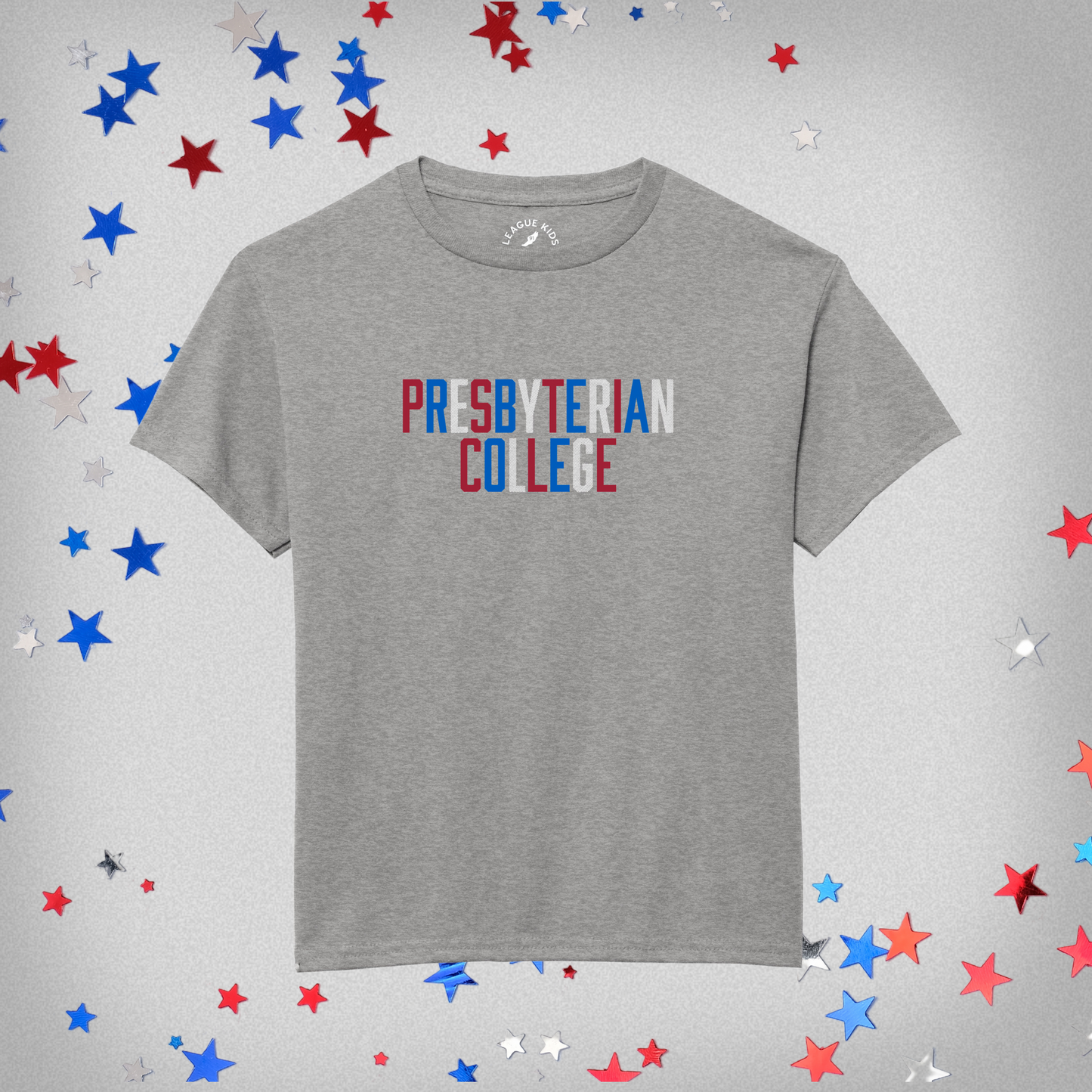 product photo of a grey youth t-shirt with presbyterian college graphic with red white and blue letters. the white letters have a subtle stripe design to them. the background of the product photo has red white and blue stars on it.
