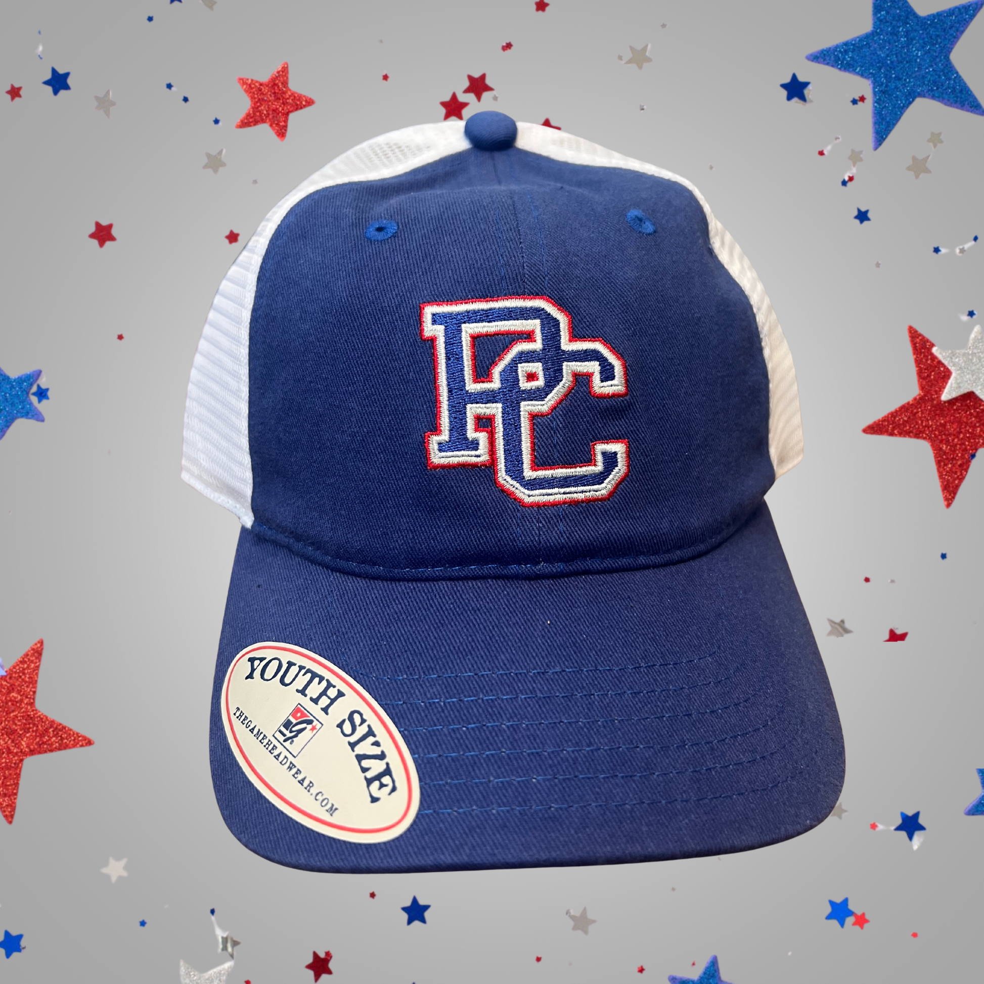 A royal blue and white trucker-style baseball cap with an embroidered 'PC' logo on the front. Set against a gray background decorated with red, white, and blue star confetti.