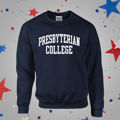 A navy blue crewneck sweatshirt with 'PRESBYTERIAN COLLEGE' printed in white arched block letters across the chest. The sweatshirt is displayed against a gray background decorated with scattered red, white, and blue glitter stars.