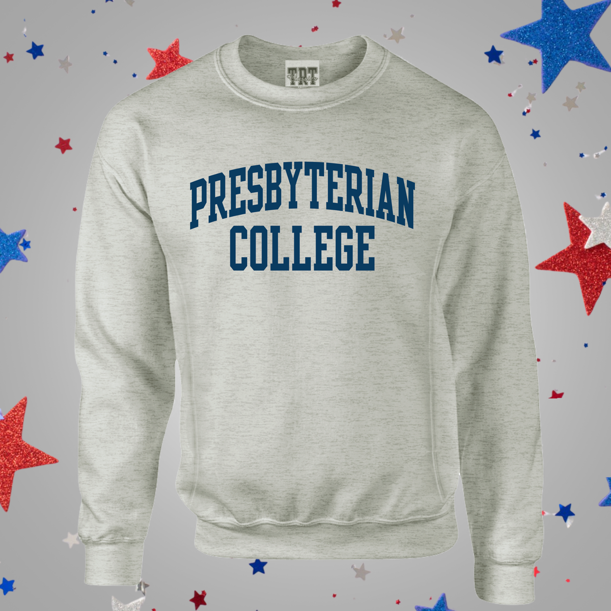 An oatmeal crewneck sweatshirt featuring the words 'PRESBYTERIAN COLLEGE' printed in a dark blue arched font on the chest. The sweatshirt is displayed against a gray background decorated with scattered red, white, and blue glitter stars.