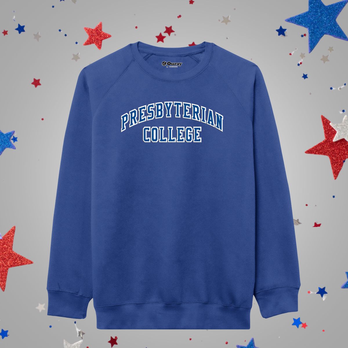 A royal blue crewneck sweatshirt featuring 'PRESBYTERIAN COLLEGE' printed in white arched block letters with a blue outline across the chest. The sweatshirt is displayed flat against a light gray background decorated with scattered red, white, and blue glitter stars.