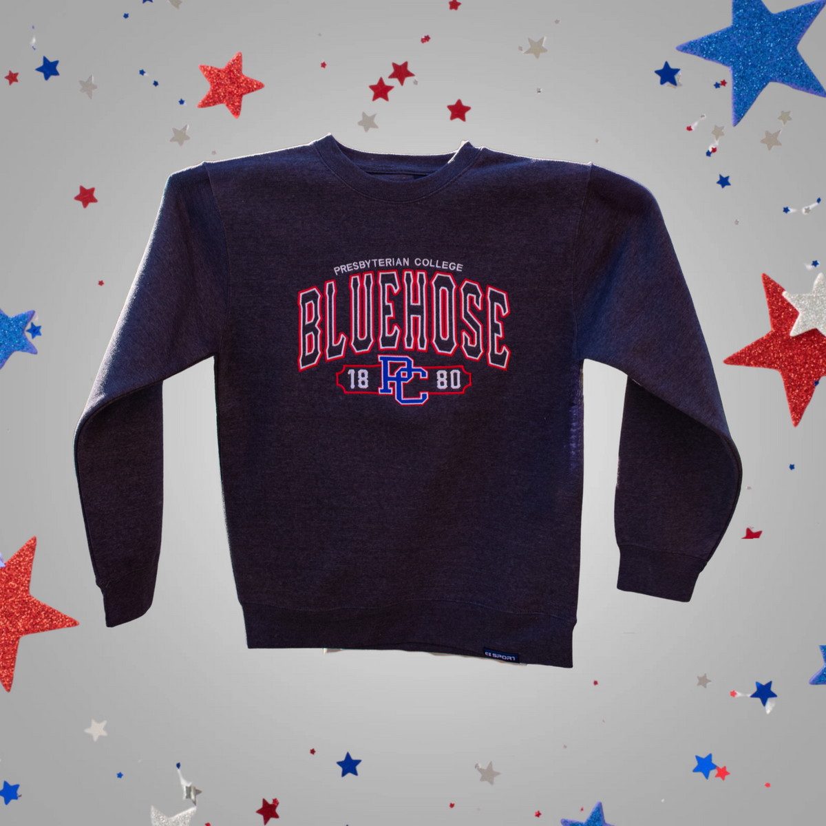 A charcoal crewneck sweatshirt featuring a red and blue 'BLUEHOSE' graphic with 'PRESBYTERIAN COLLEGE' and '18 PC 80' printed on the chest, displayed against a light gray background decorated with red, white, and blue star confetti.