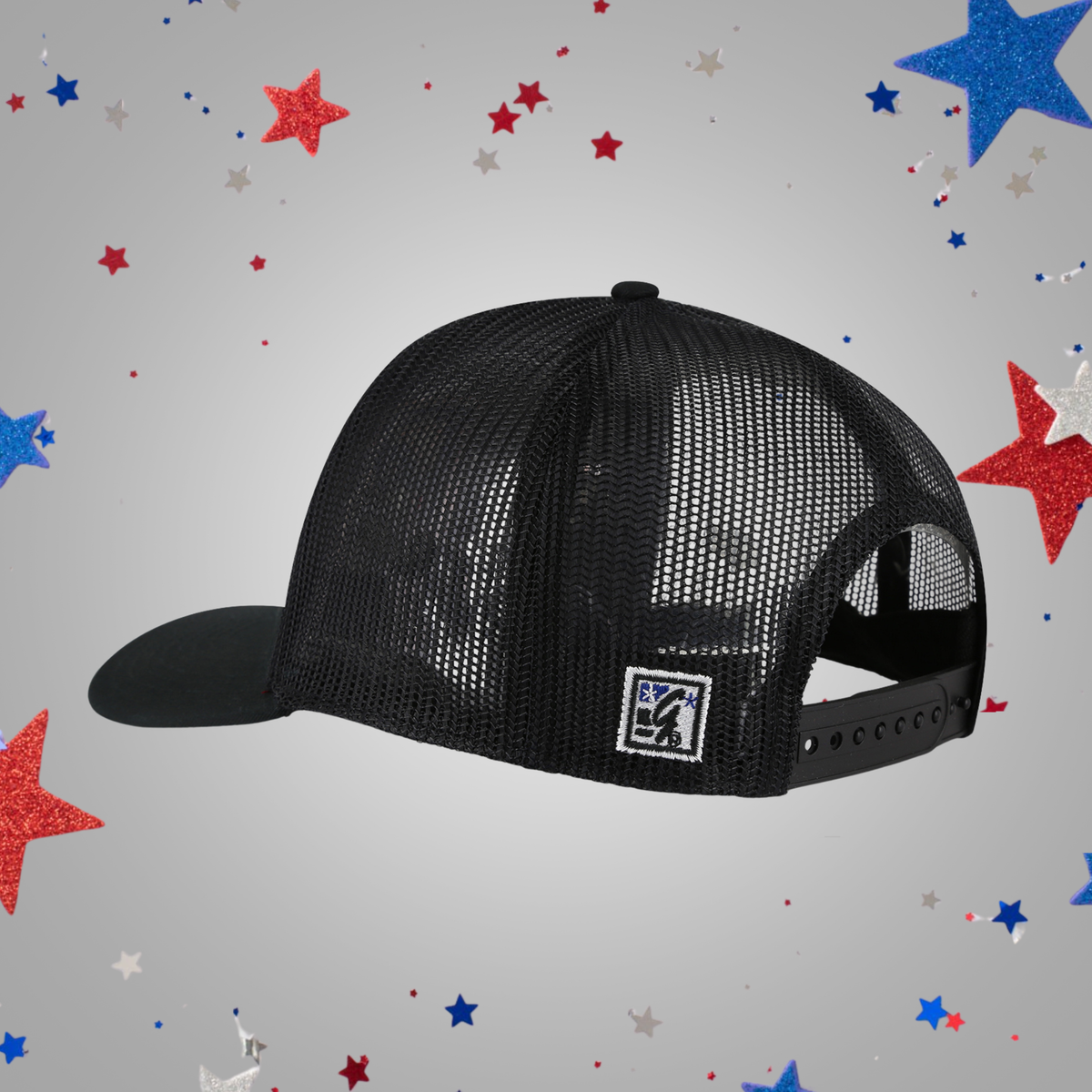 A black trucker-style mesh cap with a curved brim and a small square patch on the back, shown on a light gray background with scattered red, white, and blue star confetti.