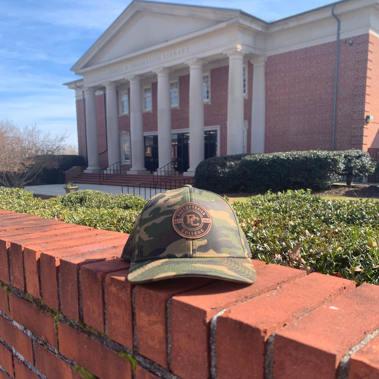 Camouflage cap with a logo on a brick ledge in front of a building